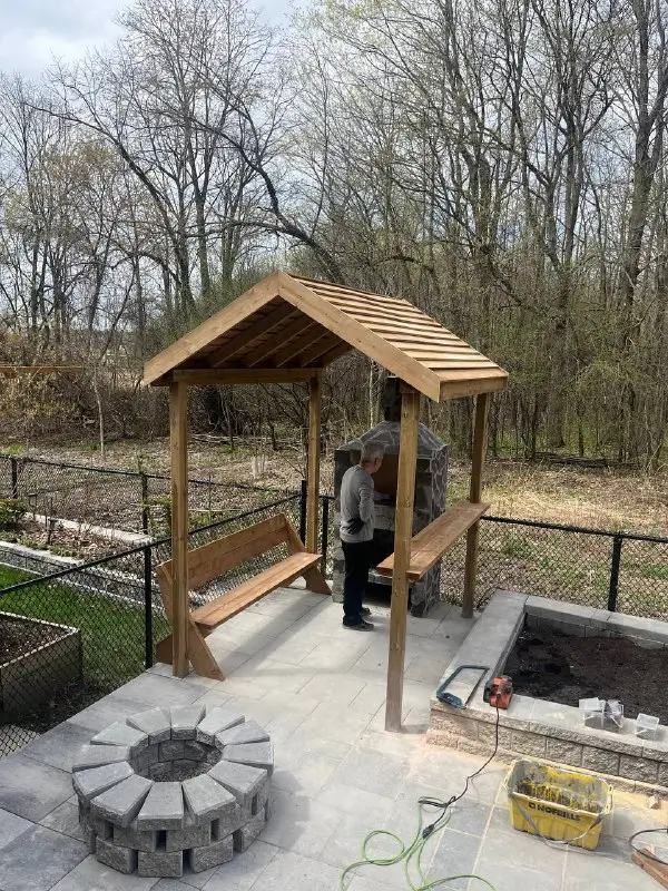 Custom wooden gazebo with built-in benches and stone firepit in a Toronto backyard